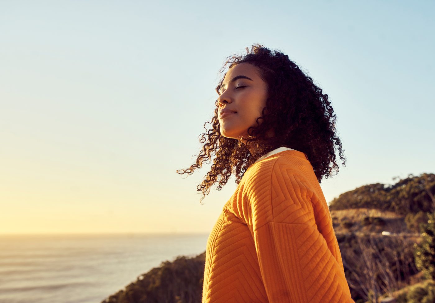 A woman outdoors with her eyes closed, face turned to the sun